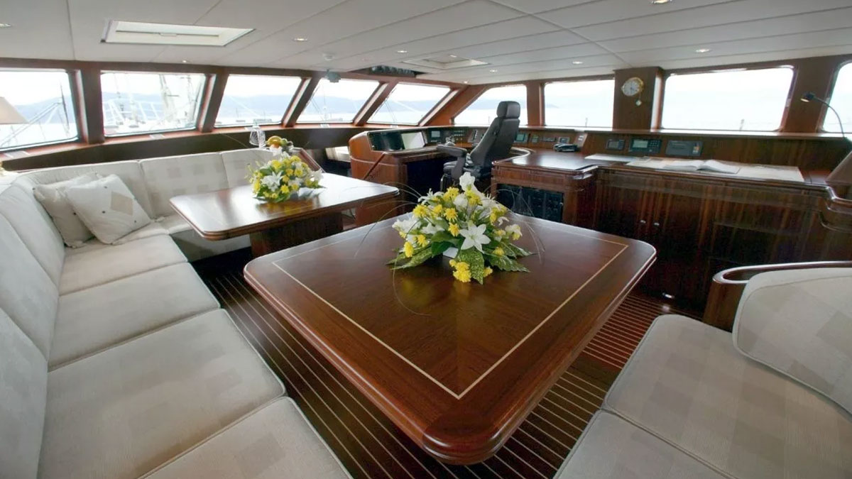 42m Jongert Infatuation sail custom yacht by Tony Castro Yachts with dark navy hull and twin masts, anchored in crystal clear turquoise waters near rocky coastline