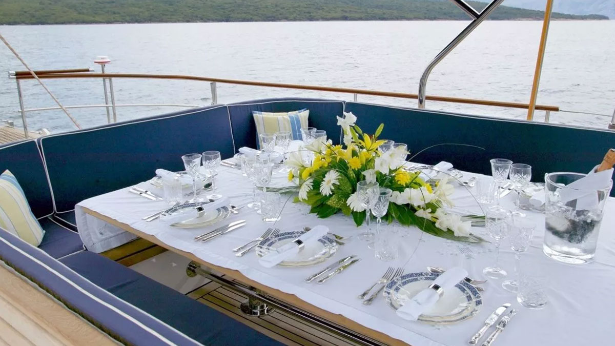 42m Jongert Infatuation sail custom yacht by Tony Castro Yachts with dark navy hull and twin masts, anchored in crystal clear turquoise waters near rocky coastline