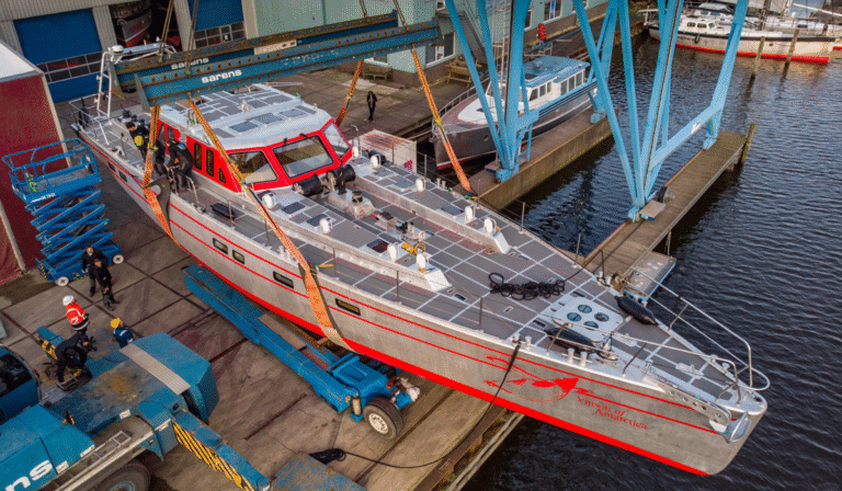 23m Pelagic 77 custom sail yacht by Tony Castro Yachts with distinctive red hull accents and three masts, sailing under full canvas on calm blue open water