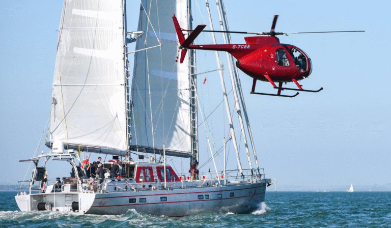 23m Pelagic 77 custom sail yacht by Tony Castro Yachts with distinctive red hull accents and three masts, sailing under full canvas on calm blue open water